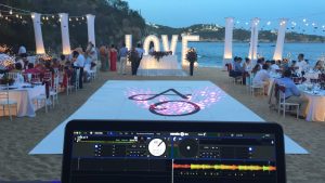 Boda en la playa al atardecer, con pista de baile, letras iluminadas de LOVE y la consola de DJ en primer plano