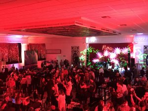 Salón iluminado en rojo con invitados frente al escenario durante un evento