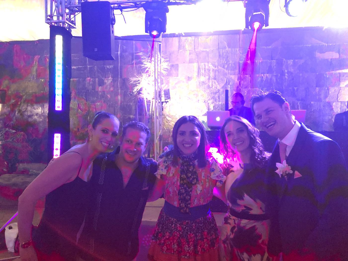 Invitados posando frente a la cabina de DJ con iluminación morada y chispero frío en un evento al aire libre