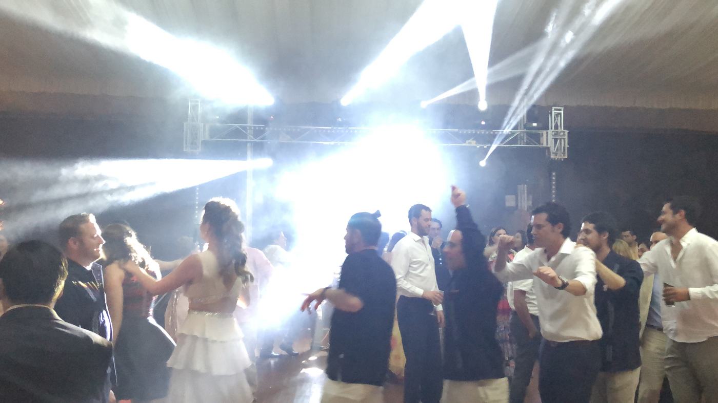 Pista de baile a reventar con haces de luz blanca y humo en una fiesta bajo carpa