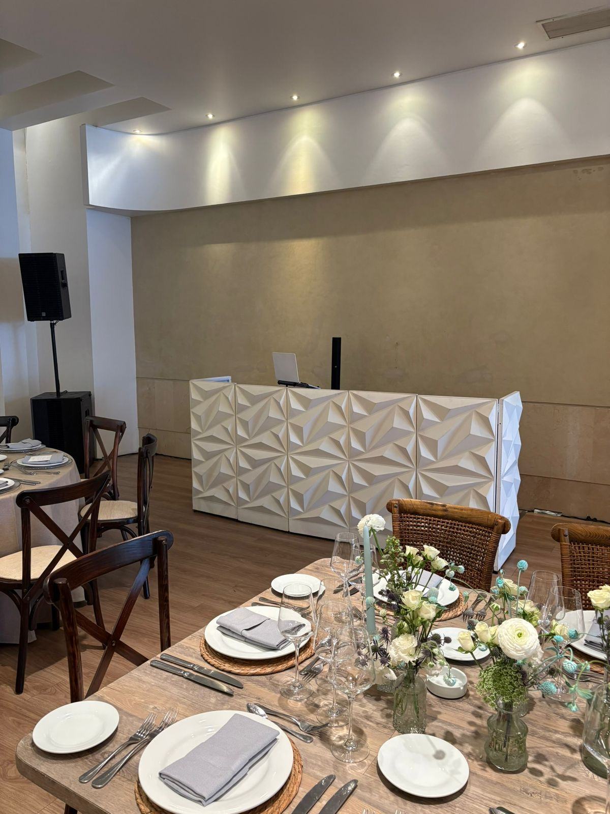 Cabina de DJ blanca con panel geométrico y bafle profesional montada en un salón antes de que llegue la gente