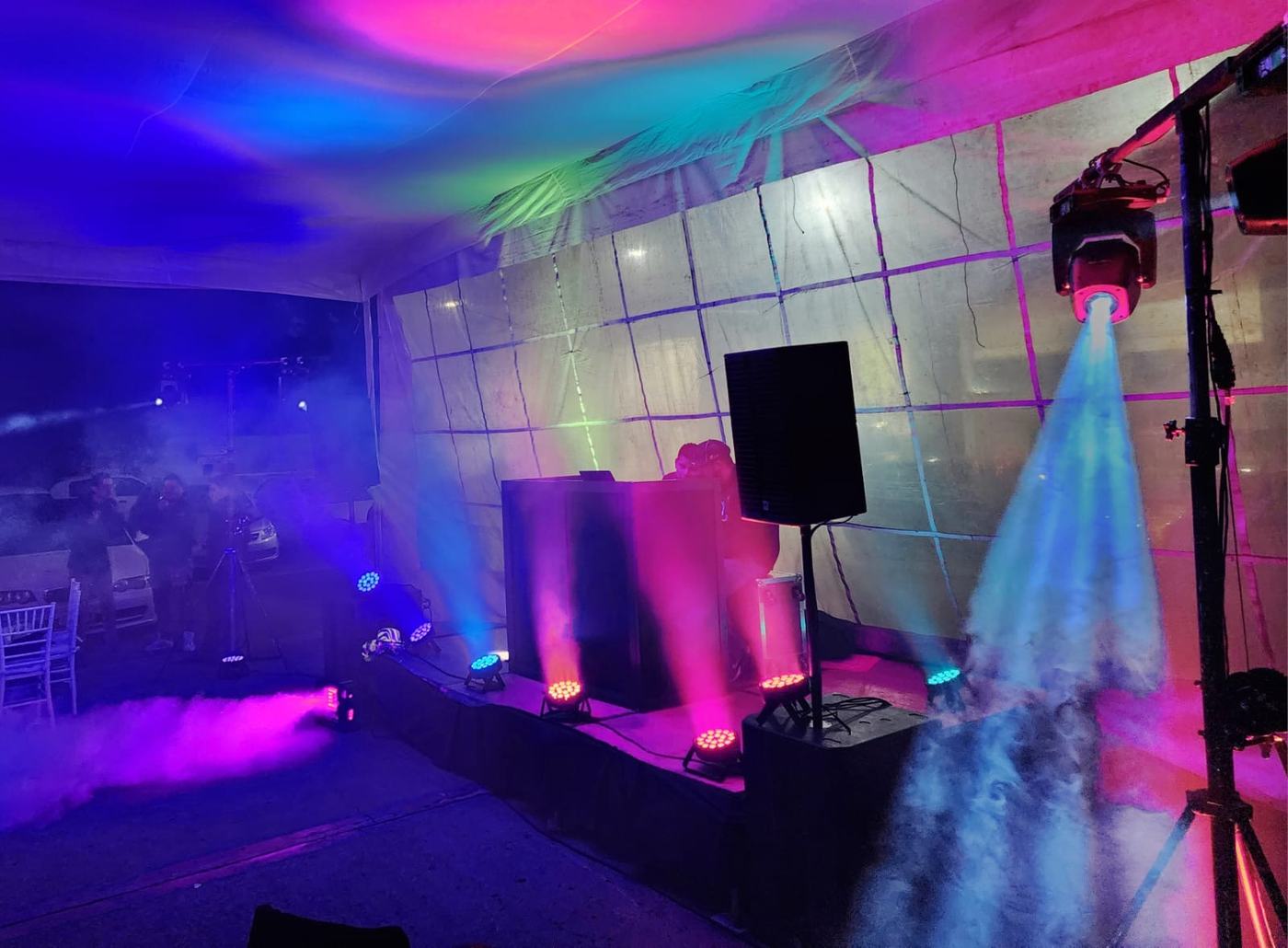 Cabina de DJ bajo carpa con luces LED de colores, máquina de humo y una luz robótica encendida