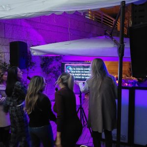 Invitadas cantando karaoke al aire libre con micrófonos inalámbricos, pantalla de letras e iluminación morada, con cabina Echoe iluminada